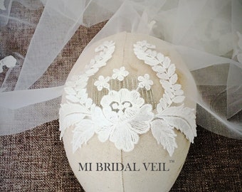 Puede incluir: Un velo de novia blanco con delicados detalles de encaje floral. El velo está drapeado sobre una cabeza de maniquí, mostrando el intrincado diseño. El encaje presenta un patrón floral con hojas y pequeñas flores. El texto "MI BRIDAL VEIL" es visible.