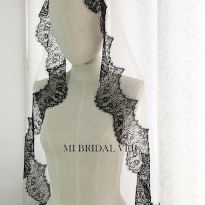 May include: A bridal veil on a mannequin. The veil is white with a black lace trim. The lace trim has a scalloped edge and is visible around the face and shoulders. The text "MI BRIDAL VEIL" is printed on the mannequin.