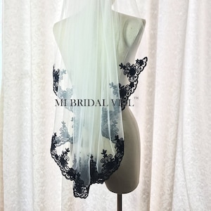 May include: A white bridal veil with a black floral lace trim. The veil is displayed on a mannequin. The text "MI BRIDAL VEIL" is visible on the veil.