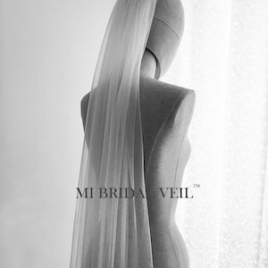 Può includere: Un velo da sposa trasparente, color avorio, è drappeggiato su un manichino. Il velo è lungo e fluente, con una consistenza morbida e delicata. Il testo "MI BRIDA VEIL" è visibile.