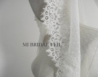 May include: A white bridal veil with delicate lace trim and a dotted pattern. The veil is draped over a mannequin, showcasing the intricate details and texture. The text "MI BRIDAL VEIL" is visible.