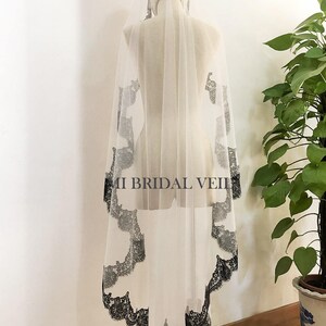 May include: A sheer white bridal veil with a delicate black lace trim and accents. The veil is displayed on a mannequin, showcasing its flowing design. The text "MI BRIDAL VEIL" is visible on the veil.