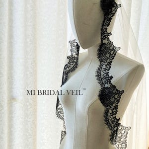May include: A white bridal veil with a delicate black lace trim. The lace features floral patterns and borders the edges of the veil. The text "MI BRIDAL VEIL" is printed on the mannequin.