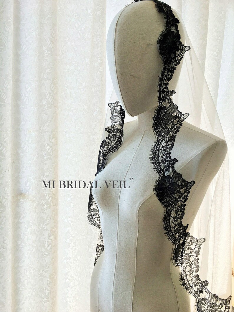 May include: A white bridal veil with a delicate black lace trim. The lace features floral patterns and borders the edges of the veil. The text "MI BRIDAL VEIL" is printed on the mannequin.