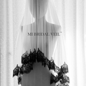 May include: A sheer white bridal veil with a black lace trim, displayed on a mannequin. The veil is long and flowing, with the text "MI BRIDAL VEIL" visible. The lace trim adds a decorative element to the veil.