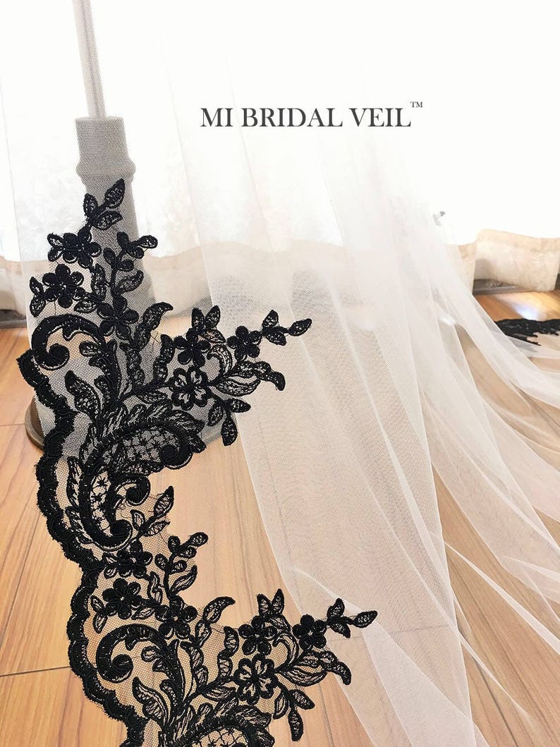 May include: A white bridal veil with a black floral lace trim. The lace features intricate designs of flowers and leaves. The text "MI BRIDAL VEIL" is visible on the veil.