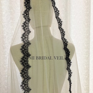 May include: A sheer white bridal veil with a delicate black lace trim. The lace trim is scalloped and runs along the edges of the veil. The text "MI BRIDAL VEIL" is visible on the veil.