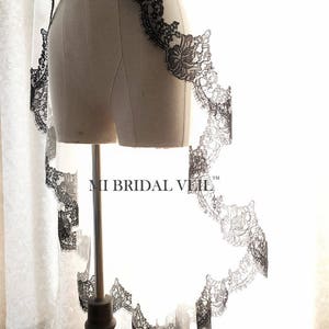 May include: A bridal veil with a delicate black lace trim. The lace features a floral pattern and borders the edge of the veil. The veil is displayed on a mannequin. The text "MI BRIDAL VEIL" is visible.