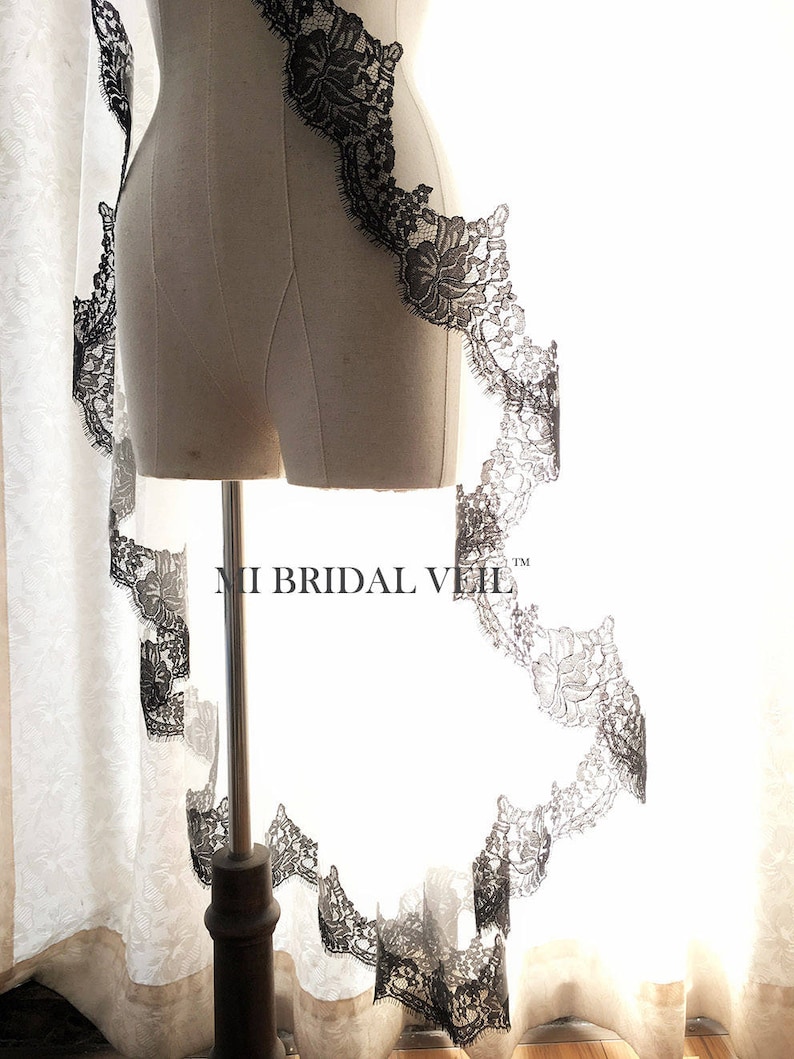May include: A bridal veil with a delicate black lace trim. The lace features a floral pattern and borders the edge of the veil. The veil is displayed on a mannequin. The text "MI BRIDAL VEIL" is visible.