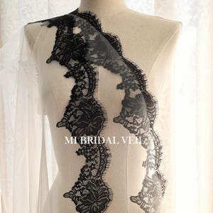 May include: A bridal veil with a delicate black lace trim. The lace features intricate floral patterns and a scalloped edge. The veil is displayed on a mannequin, showcasing its design and texture. The text "MI BRIDAL VEIL" is visible.