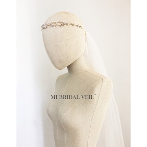 Può includere: Un cerchietto da sposa dorato con un delicato design a vite ornato di cristalli scintillanti. È abbinato a un velo bianco trasparente. Il testo "MI BRIDAL VEIL" è visibile.