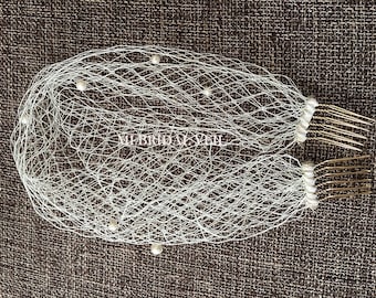May include: A white bridal veil with a net design, adorned with small pearls. The veil has two combs for secure placement in the hair. The text "MI BRIDAL VEIL" is visible on the veil.