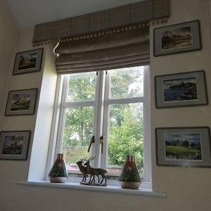May include: A window featuring framed landscape paintings, a decorative valance, and a window treatment. The window sill displays two decorative vases, and a deer figurine. The window overlooks a green, leafy landscape.