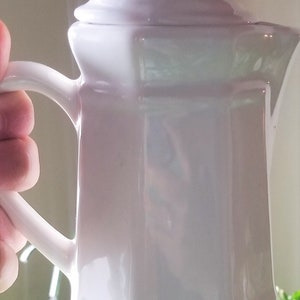 Puede incluir: Una tetera de cer&aacute;mica blanca con tapa y asa. La tetera tiene un cuerpo redondeado y una base cuadrada.