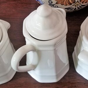 Puede incluir: Tres juegos de az&uacute;car y crema de cer&aacute;mica blanca con tapas. La crema tiene un asa. El azucarero tiene una tapa con un pomo en la parte superior. La crema y el azucarero tienen una forma octogonal.