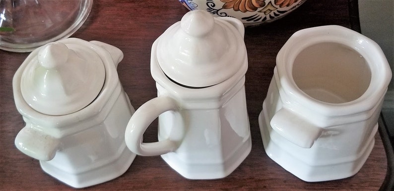 Puede incluir: Tres juegos de az&uacute;car y crema de cer&aacute;mica blanca con tapas. La crema tiene un asa. El azucarero tiene una tapa con un pomo en la parte superior. La crema y el azucarero tienen una forma octogonal.