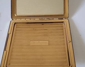 May include: A gold-colored compact mirror with a hinged lid and a mirror inside. The compact has a raised inscription that reads "Esprit de Paris, Made in France".