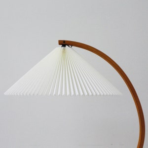 K&ouml;nnte beinhalten: Ein wei&szlig;er, gefalteter Lampenschirm h&auml;ngt an einer Bogenlampe aus Holz. Der Lampenschirm ist aus Papier und hat ein filigranes, gefaltetes Design.