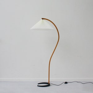 K&ouml;nnte beinhalten: Eine gebogene Stehlampe aus Holz mit einem wei&szlig;en, gefalteten Lampenschirm und einem schwarzen Fu&szlig;.