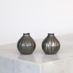 May include: Two small, silver, onion-shaped vases with a ribbed design.