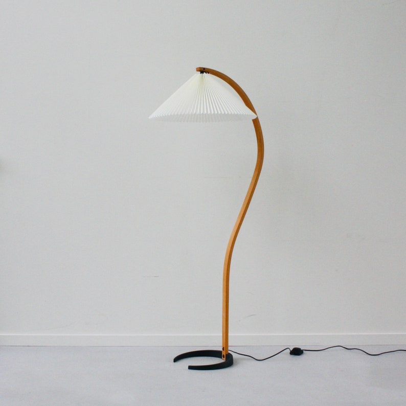 K&ouml;nnte beinhalten: Eine gebogene Stehlampe aus Holz mit einem wei&szlig;en, gefalteten Lampenschirm und einem schwarzen Fu&szlig;.