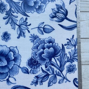 May include: A square ceramic tile with a blue and white floral pattern. The tile has a silver border.
