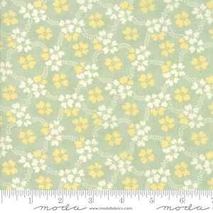 Op de afbeelding: Een stof met een herhalend bloemenpatroon. Het ontwerp toont gele en witte bloemen op een lichtgroene achtergrond. De bloemen zijn gerangschikt in een vloeiend, rankachtig patroon. Langs de onderkant is een liniaal te zien.