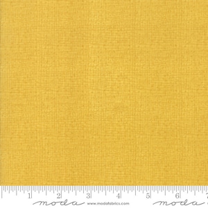 May include: A close-up of a yellow fabric with a subtle textured pattern. The fabric is measured with a ruler that reads "moda" and includes the website address "www.modafabrics.com".