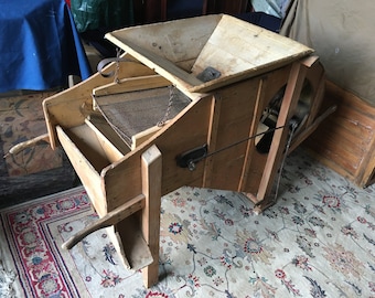 May include: Antique wooden grain separator with a metal screen and a crank handle. The separator has a wooden hopper and a wooden base.