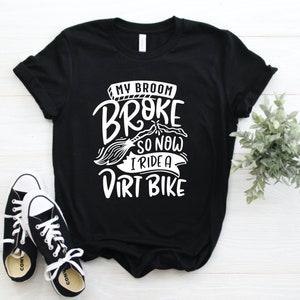 May include: Black t-shirt with white text that reads "My broom broke so now I ride a dirt bike".