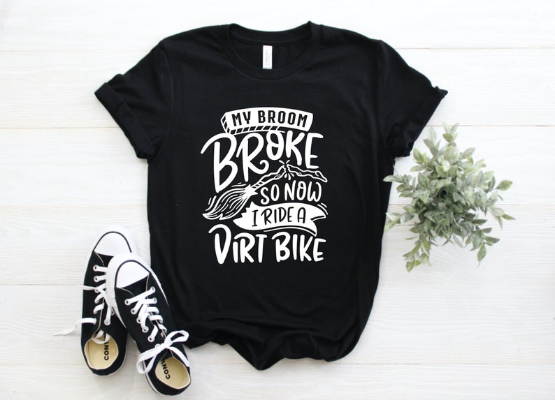 May include: Black t-shirt with white text that reads "My broom broke so now I ride a dirt bike".