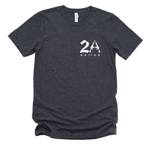 May include: A dark heather grey t-shirt with a white graphic of two rifles forming the letter 'A' with the number '2' in front of it. The graphic also includes the text '1776' and five stars.