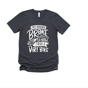 May include: Dark heather grey t-shirt with white text that reads "My broom broke so now I ride a dirt bike".