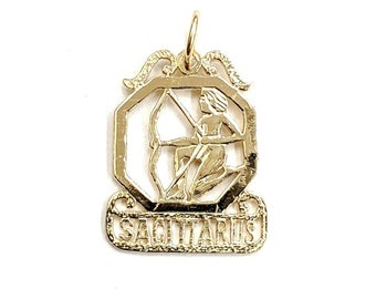 May include: Gold-toned Sagittarius zodiac sign pendant with an intricate design. The pendant features a detailed image of a centaur holding a bow and arrow, surrounded by a decorative frame. The word "Sagittarius" is inscribed on a banner below the image.