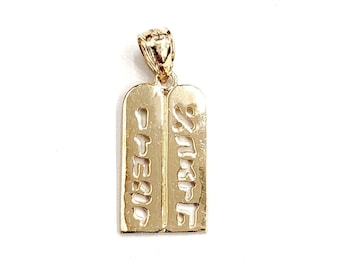May include: A gold-colored pendant featuring two rectangular tablets with Hebrew text. The pendant has a decorative bail at the top for a chain. The tablets are side-by-side, with the Hebrew letters cut out of the gold.
