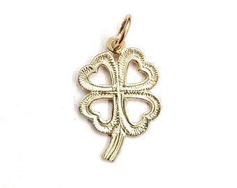 May include: A gold four-leaf clover charm with a detailed design. The charm has a loop at the top for attaching to a necklace or bracelet.