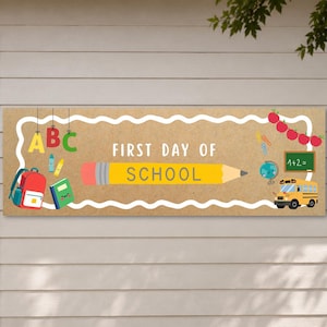 May include: A rectangular banner with a tan background and a white scalloped border. The text FIRST DAY OF SCHOOL is centered with a large yellow pencil graphic. Illustrations include a red backpack, green book, globe, school bus, and apples.