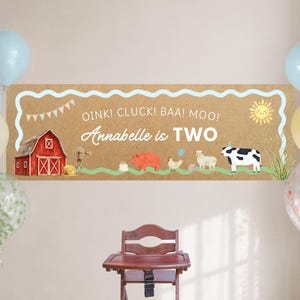 May include: A rectangular banner with a tan background featuring a red barn, a windmill, a pig, a chicken, a sheep, a cow, and a smiling sun. The text reads OINK! CLUCK! BAA! MOO! Annabelle is TWO. The banner is framed by a light blue wavy border.