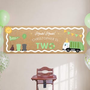 Op de afbeelding: Een rechthoekige verjaardagsbanner met een bruine achtergrond, voorzien van een groene vuilniswagen, een groene ballon met het cijfer 2, afvalbakken en een zon. De tekst luidt Honk! Honk! CHRISTOPHER IS TWO met een recyclingsymbool en vlaggetjes.