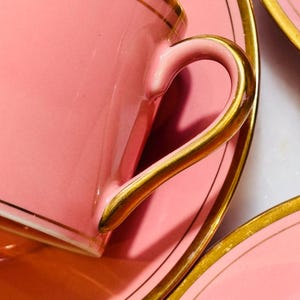 Pu&ograve; includere: Un set da t&egrave; rosa con bordo dorato. La tazza ha un manico delicato e il piattino ha un bordo largo.