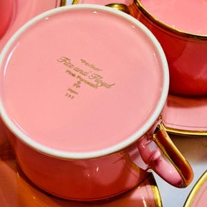 Pu&ograve; includere: Un set da t&egrave; rosa con piattino e bordo dorato. La tazza da t&egrave; ha le parole "Fitz and Floyd" e "Fine Porcelain" stampate sul fondo. Il piattino ha un bordo dorato.