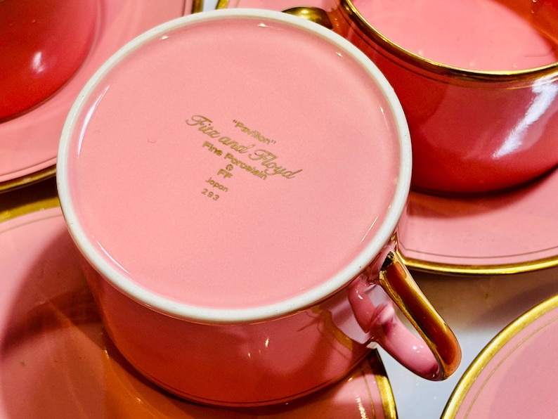 Pu&ograve; includere: Un set da t&egrave; rosa con piattino e bordo dorato. La tazza da t&egrave; ha le parole "Fitz and Floyd" e "Fine Porcelain" stampate sul fondo. Il piattino ha un bordo dorato.