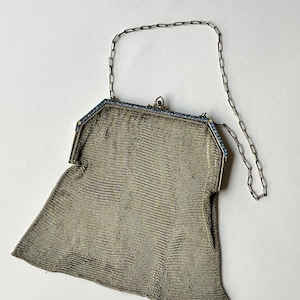 Può includere: Una borsa da sera in rete argentata con una tracolla a catena e dettagli in smalto blu.