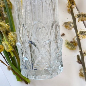 May include: A clear glass vase with a textured, geometric design. The vase has a wide mouth and a narrow base.
