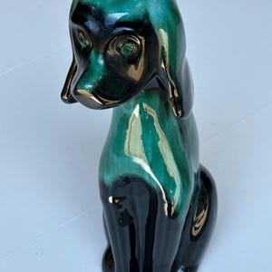 May include: A ceramic dog figurine in a seated position. The dog has a glossy finish with a color gradient of teal and black. Gold accents are on the ears, nose, and eyes. The figurine is a decorative item.