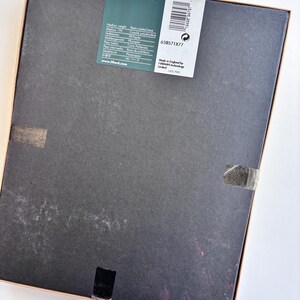 Peut inclure: Une bo&icirc;te rectangulaire avec un couvercle gris fonc&eacute; et un cadre marron clair. Une &eacute;tiquette blanche avec du texte noir et un code-barres est appos&eacute;e sur le couvercle. L'&eacute;tiquette comprend le mot "PERLA". La bo&icirc;te est scell&eacute;e avec du ruban adh&eacute;sif transparent.