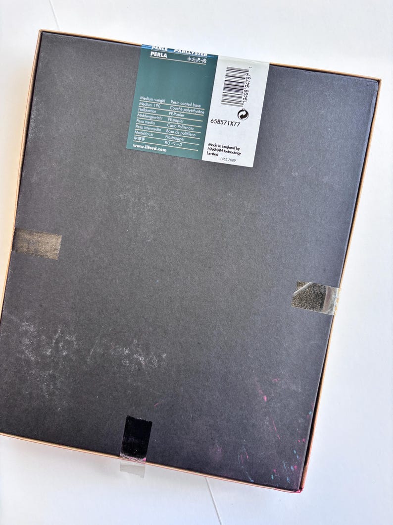 Peut inclure: Une bo&icirc;te rectangulaire avec un couvercle gris fonc&eacute; et un cadre marron clair. Une &eacute;tiquette blanche avec du texte noir et un code-barres est appos&eacute;e sur le couvercle. L'&eacute;tiquette comprend le mot "PERLA". La bo&icirc;te est scell&eacute;e avec du ruban adh&eacute;sif transparent.