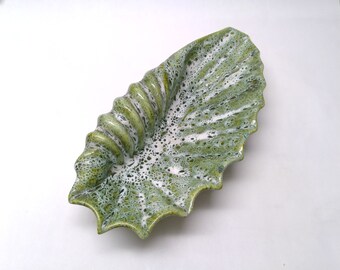 Peut inclure: Un plat en céramique vert et blanc en forme de coquille. Le plat a une surface texturée et un bord festonné.