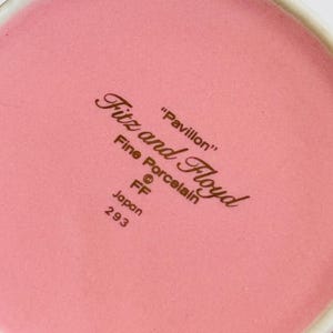 Pu&ograve; includere: Primo piano del fondo di una tazza in ceramica rosa con il testo "Fitz and Floyd" in lettere marroni. Il testo "Pavillon" &egrave; anche in lettere marroni. Il testo "Fine Porcelain" &egrave; in lettere marroni. Il testo "FF" &egrave; in lettere marroni. Il testo "Japan 293" &egrave; in lettere marroni.