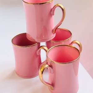 Pu&ograve; includere: Set di quattro tazze in ceramica rosa con bordo dorato. Le tazze hanno una forma arrotondata e un manico.